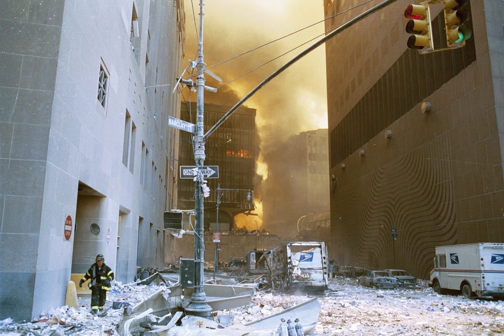 view south from the intersection of Barclay and West Broadway. WTC7 is to the right and WTC5 is the burning building on the left at the end of the street. The Postal Building is on the left. The Postal truck on the left side of the street nearest the camera appears fairly 'eaten up' on its left side, while the Postal truck on the right side of the street appears to be undamaged.